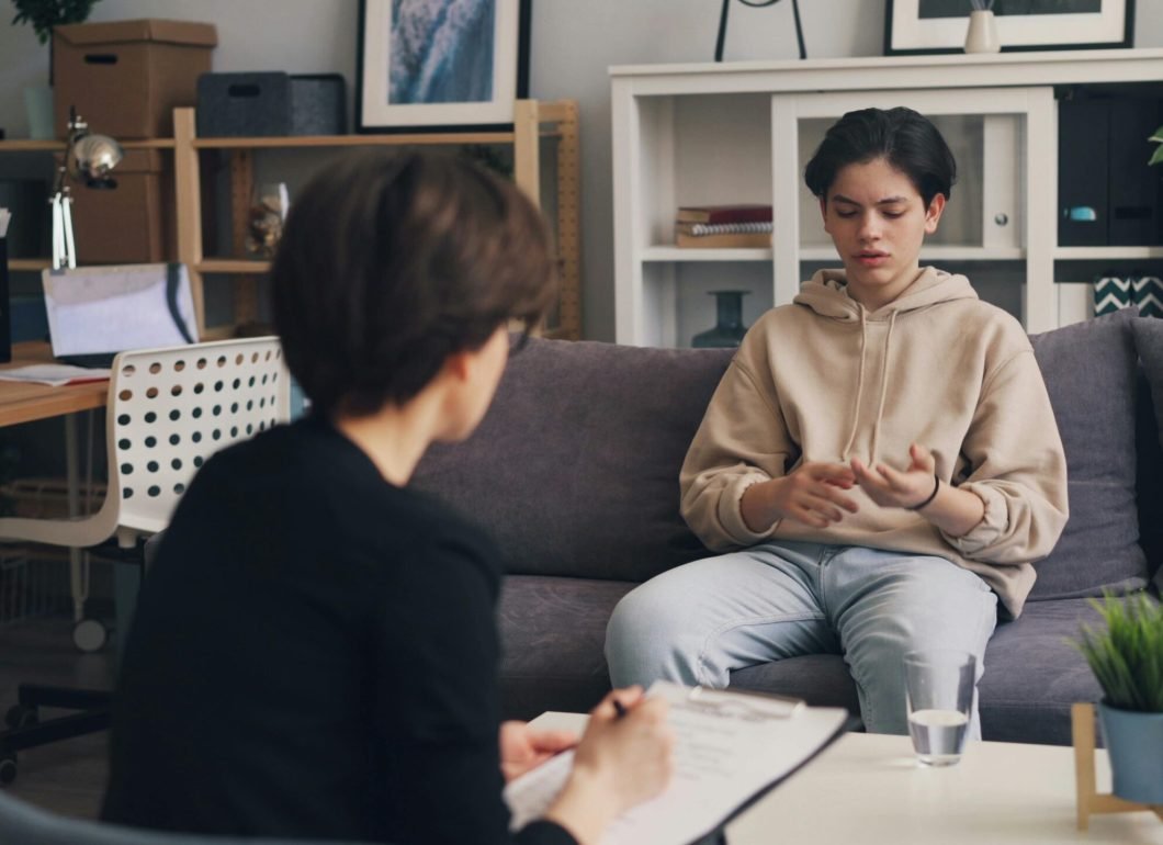 pexels-photo-23496574-23496574 A teenager engages in a therapy session with a professional counselor in a modern office setting.