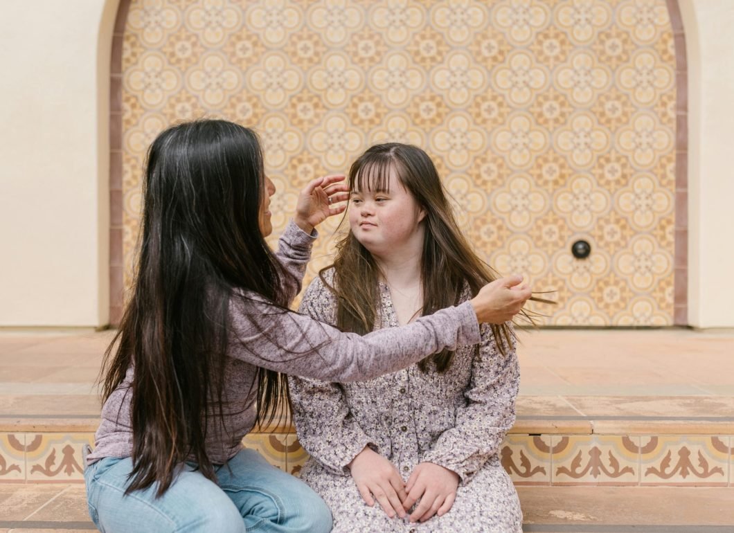 pexels-photo-7403040-7403040-1 A mother lovingly adjusts her daughter's hair as they sit together on steps.