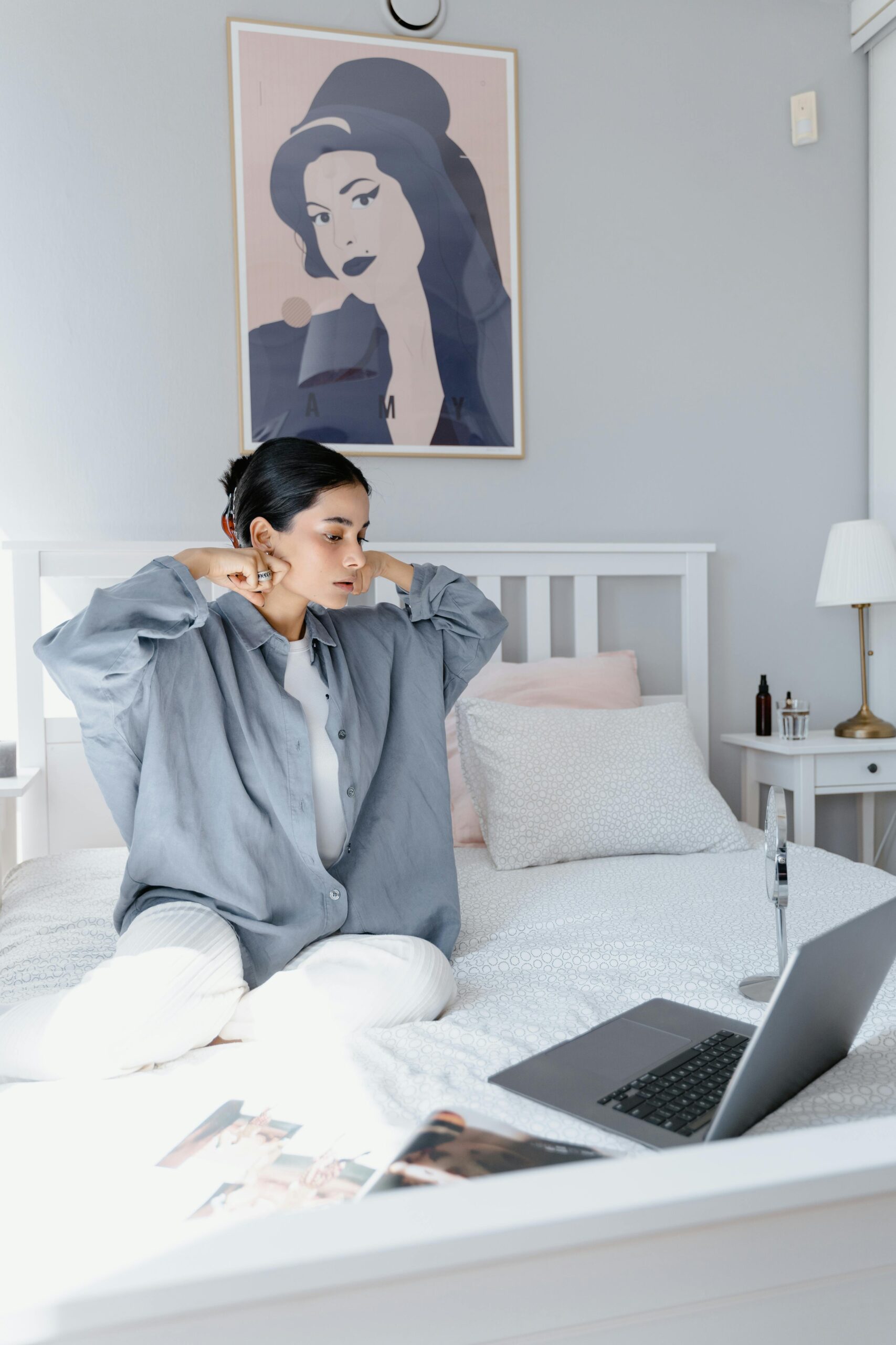 Woman sitting on bed in stylish bedroom, using laptop for work or leisure.