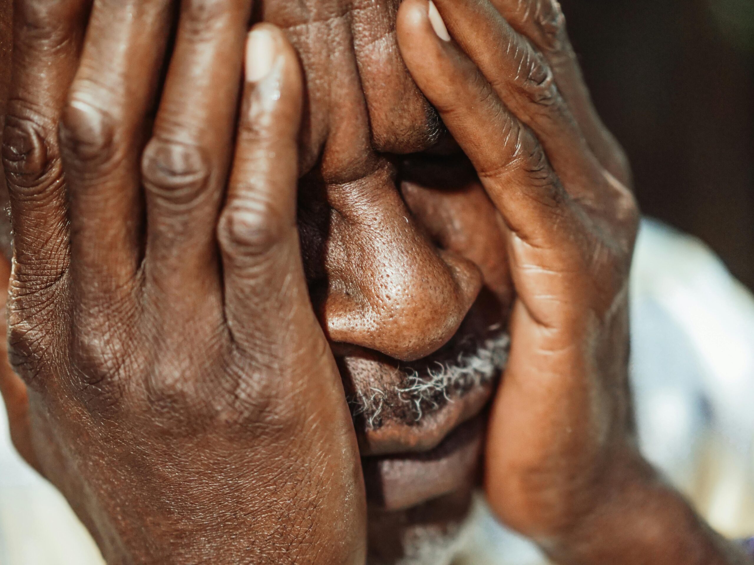 Close-up portrait of an elderly man with hands covering face, showing emotion.