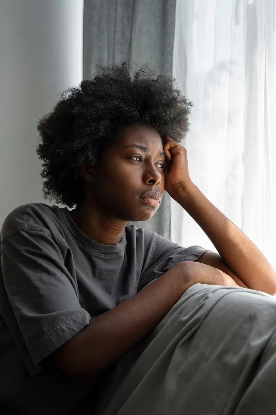 Woman sitting by a window dealing with chronic anxiety and stress at Mentally Healthy Care in Long Beach, CA.