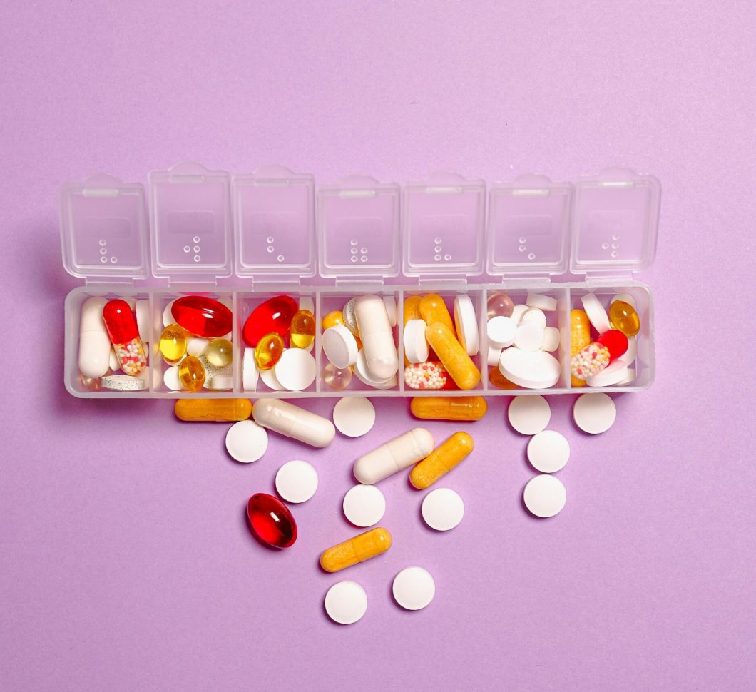 A daily pill organizer filled with various pills and capsules on a purple background. Ideal for healthcare topics.